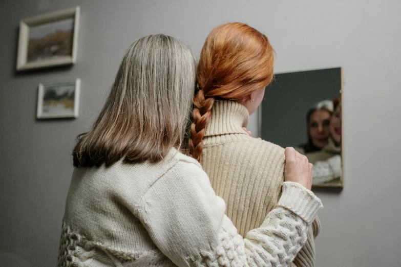 two women look at each other as they stand in front of a mirror