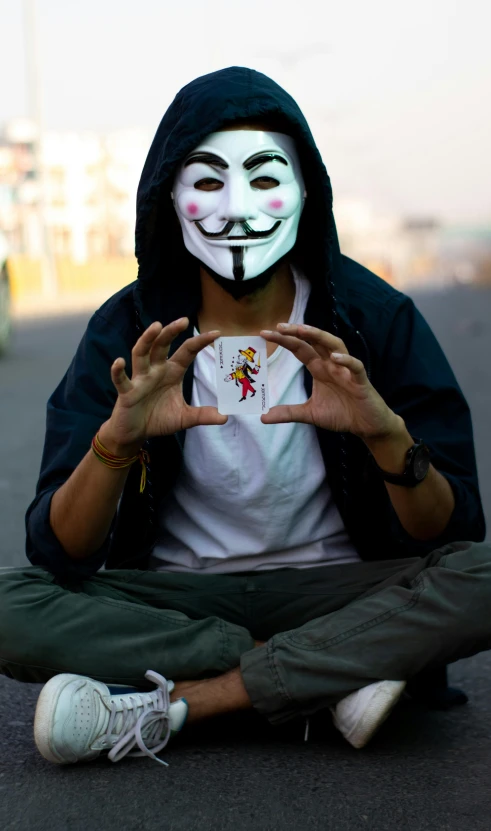 a man wearing a white mask sitting in the middle of a street