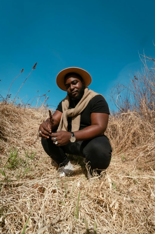 a man kneeling on the ground in a hat