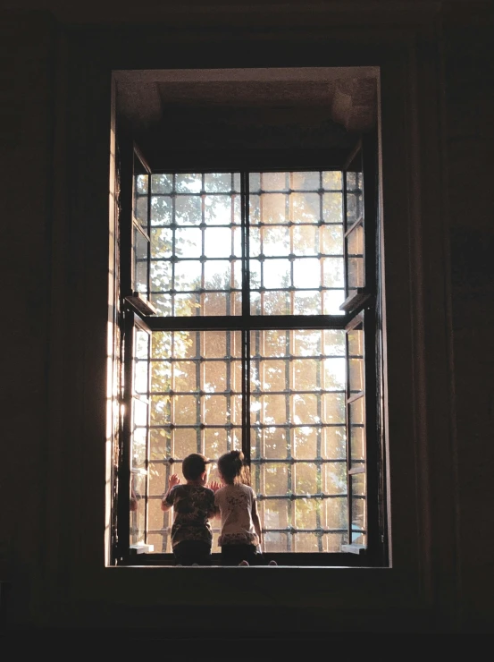 two little girls looking out of a window with the sunlight shining through