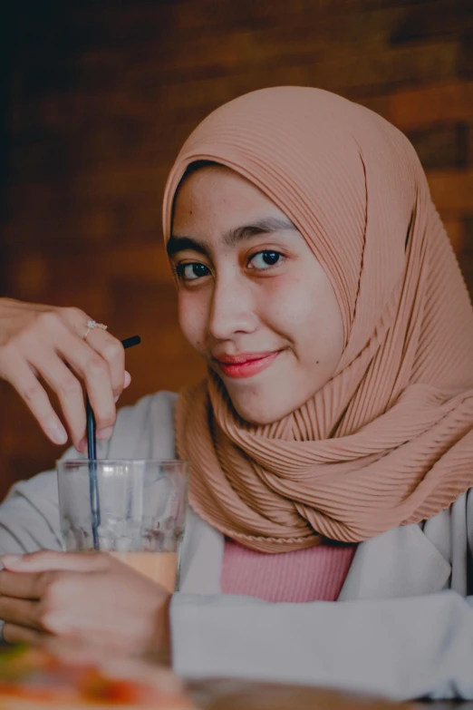 a woman wearing a hijab smiles while holding an empty glass