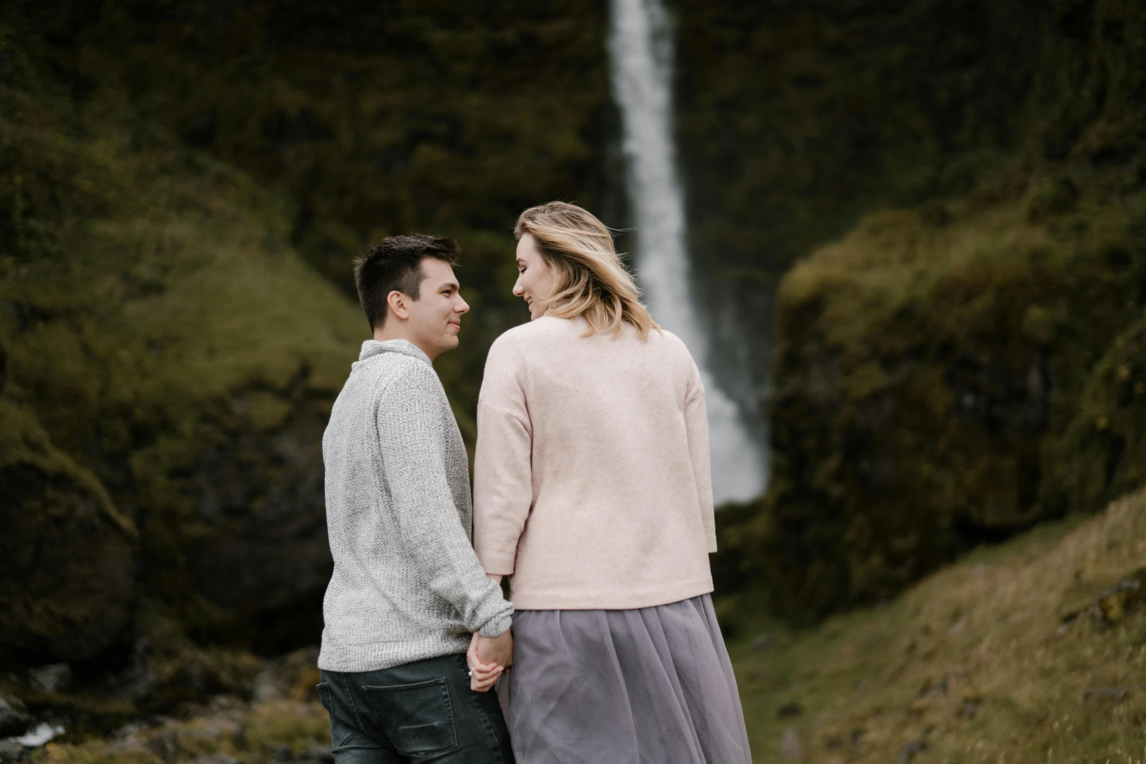 a couple holding hands and looking at each other near a waterfall