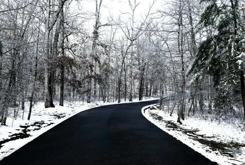 an empty road surrounded by snow covered trees