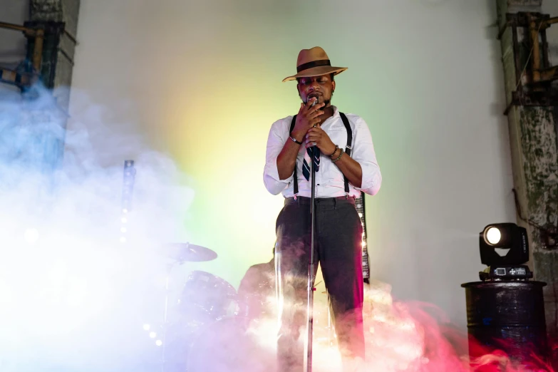 a man in a hat and suspenders stands in front of a microphone