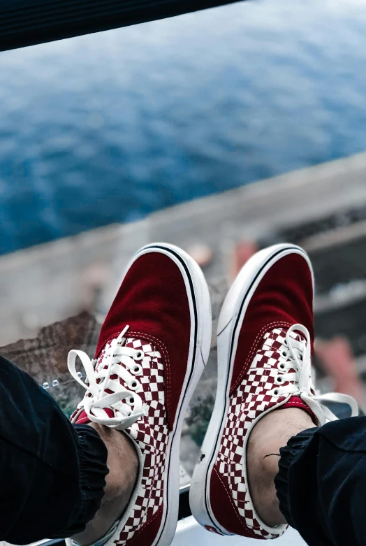 a person wearing red and white sneakers standing on the edge of a dock