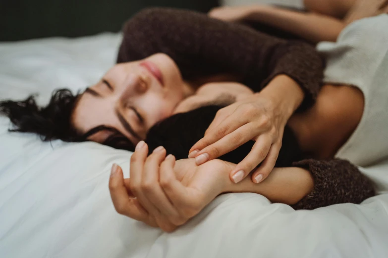 two women are holding hands on the bed