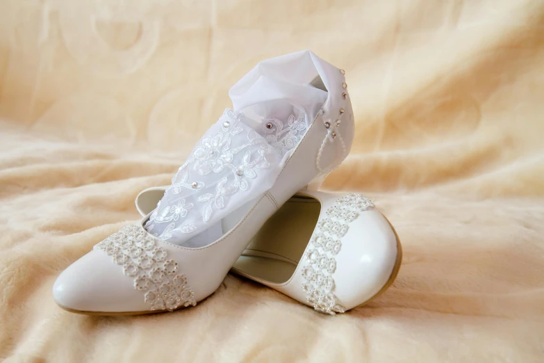 two pairs of womens white wedding shoes on a bed