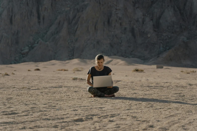 a woman sitting in the sand with a laptop