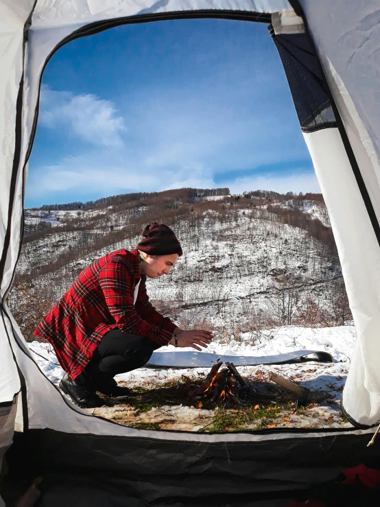 a person crouching down in front of a tent set up in the snow