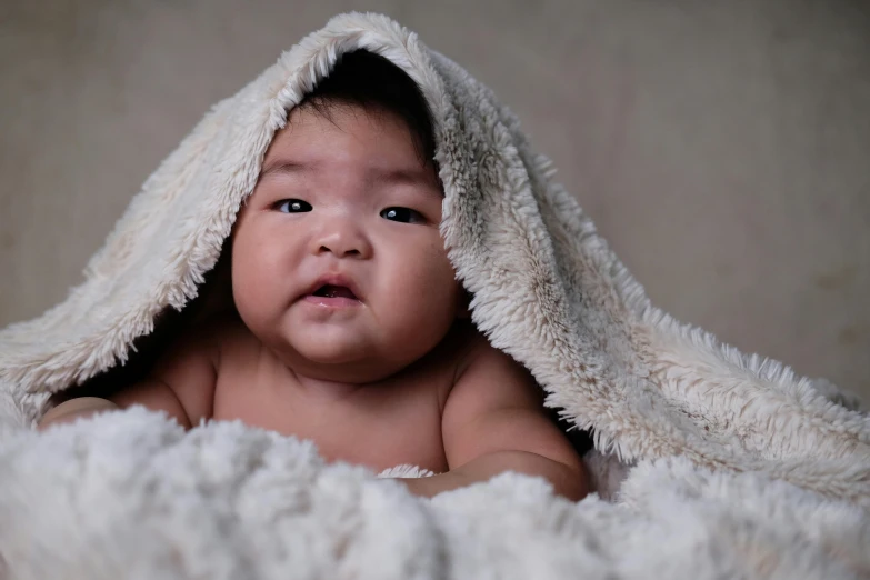 an infant laying underneath a blanket with eyes wide open