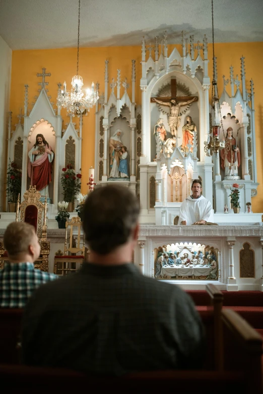 people in chairs near a altar, with statues on the wall