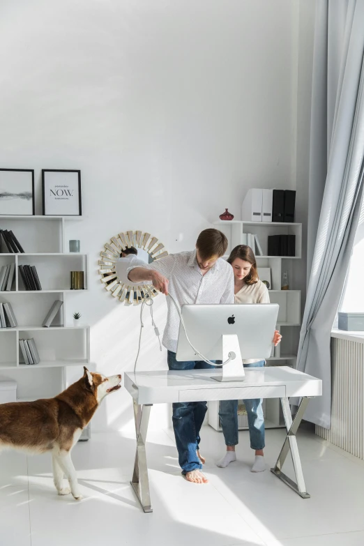 there are a  and girl sitting at the computer desk with a dog nearby