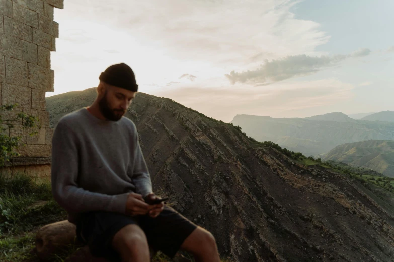 a man sits on the side of a cliff looking at his phone