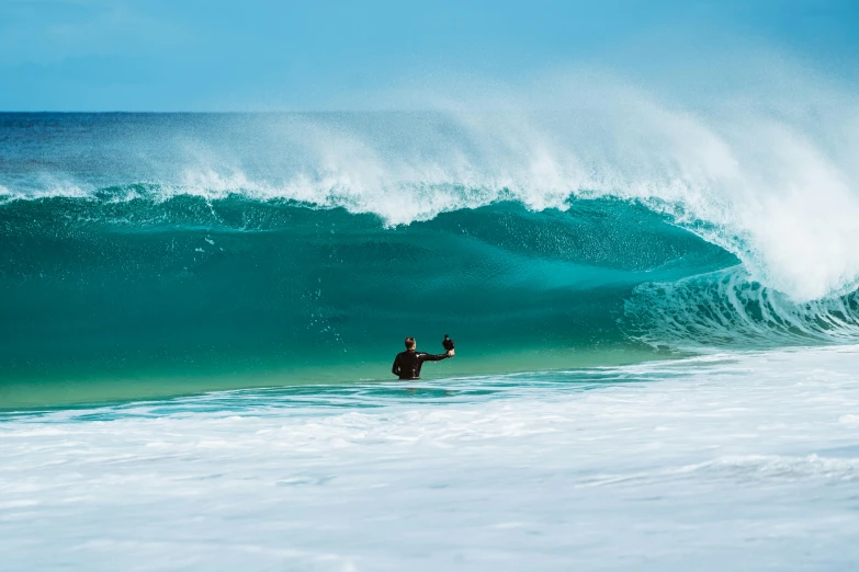 a person in the ocean with their arm out, holding up a hand as a large wave approaches