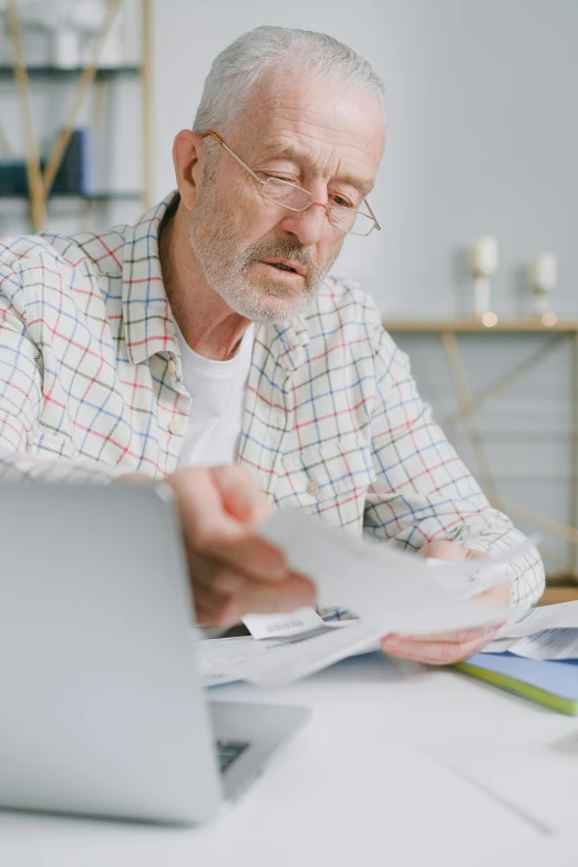 an old man looking at a document and using a laptop