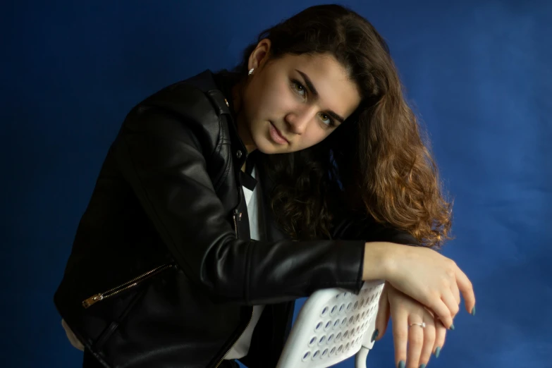 a woman in a black jacket posing next to a white chair