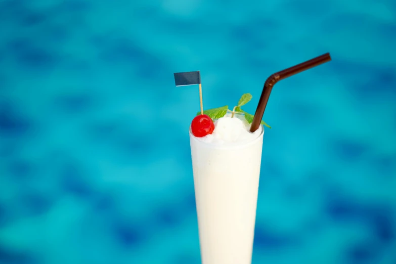 a white milk shake with cherry garnish, red flower and green straw