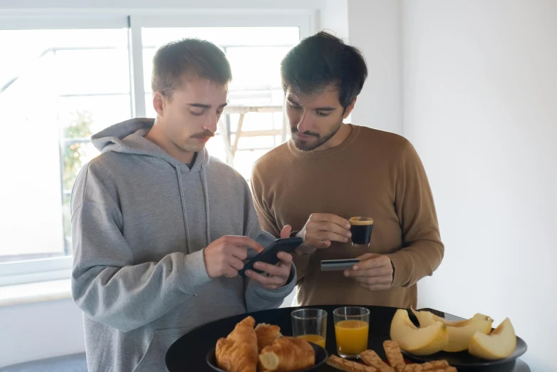 two men are looking at their phones as they prepare food