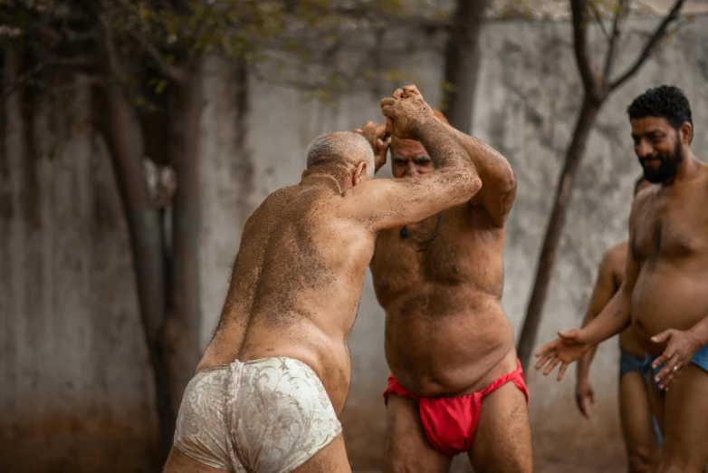 two men wrestling in a dirty field while another looks on