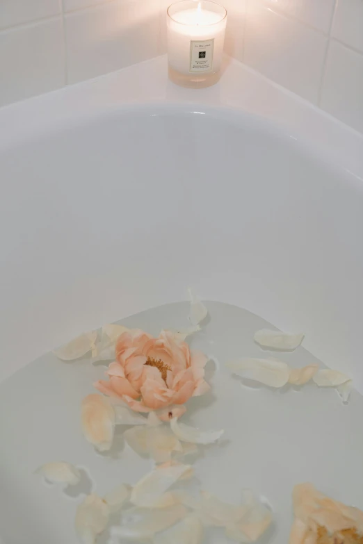 a flower laying in water next to a candle