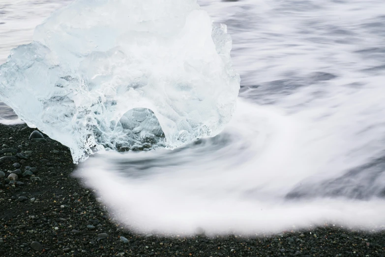 a single ice cube on black rocks near the water