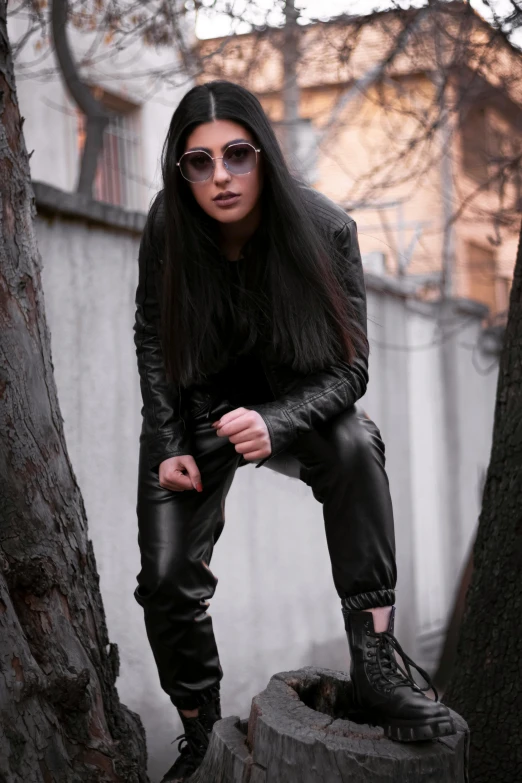 a woman wearing black leather sitting on top of a tree stump