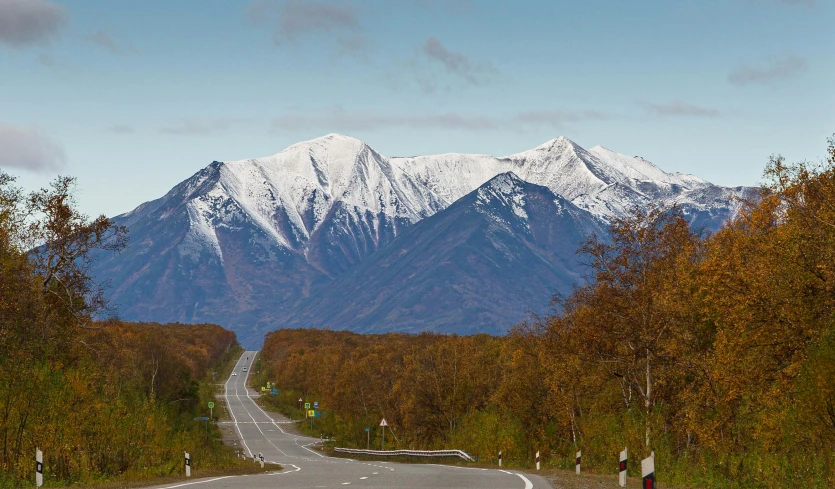 the view of a country road leading towards a huge snow capped mountain