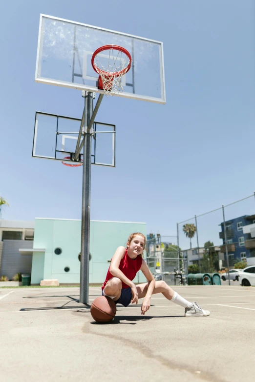 a girl kneeling by a basketball hoop on the ground