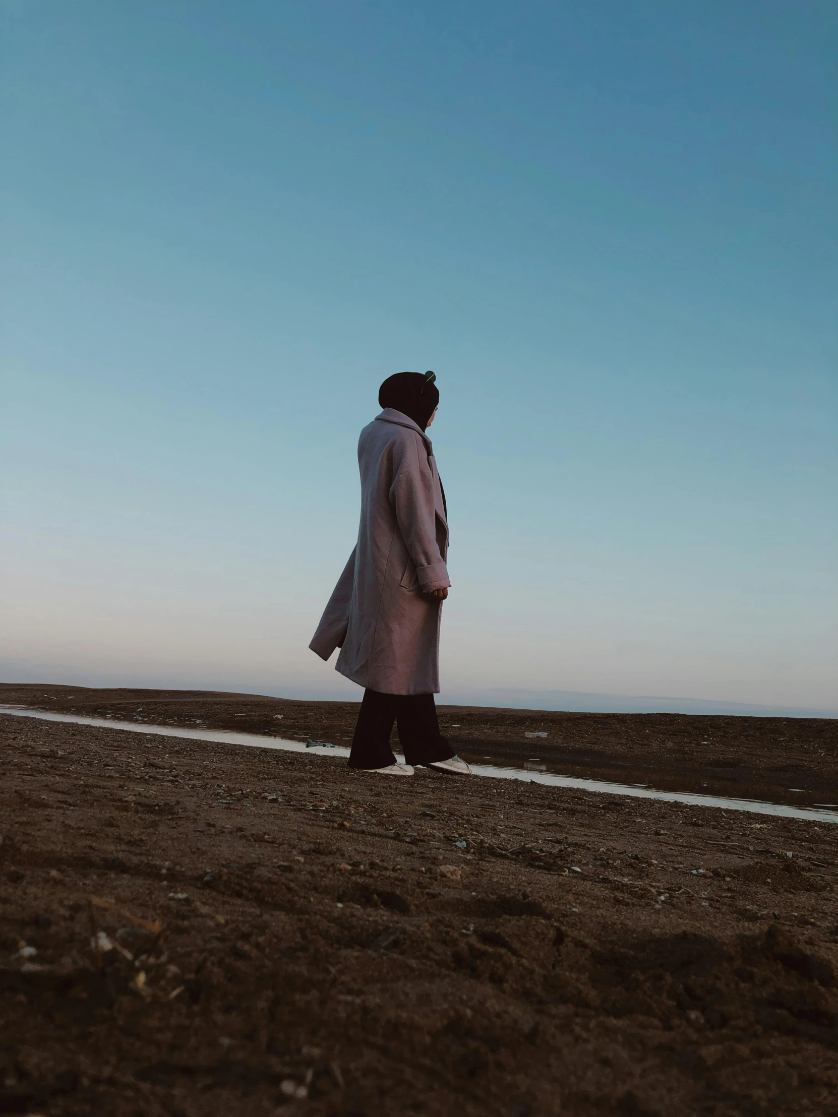 a man with a hat and coat standing on a patch of land