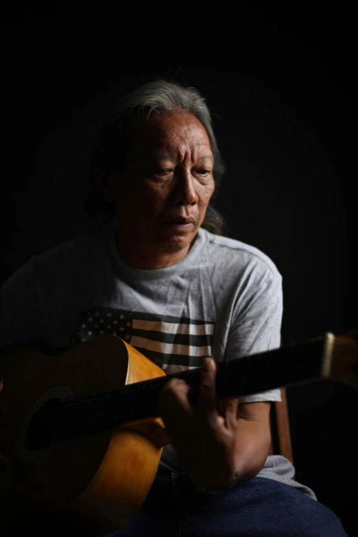 an older man sitting down playing the guitar