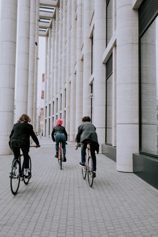 four people riding bicycles along the sidewalk between tall buildings