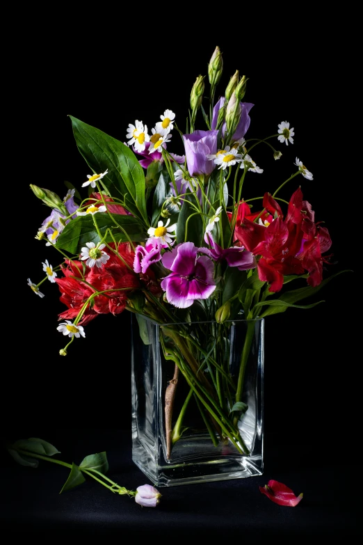 a square vase filled with assorted flowers on top of a black surface