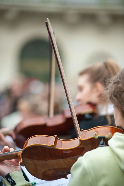 a woman playing violin outside while someone looks on