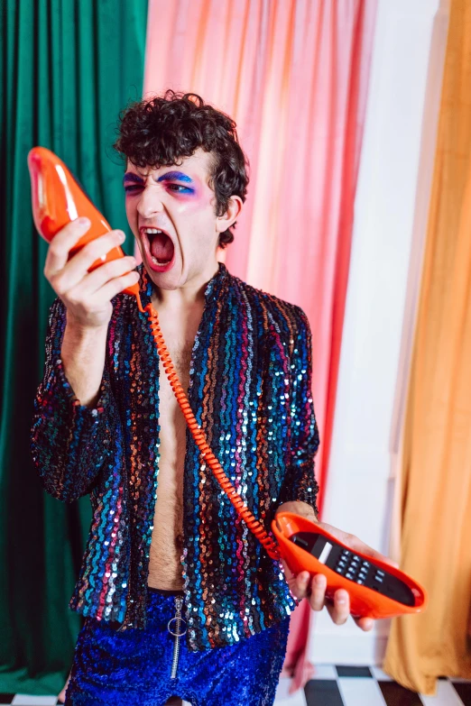 a man holding an orange flip phone next to his mouth