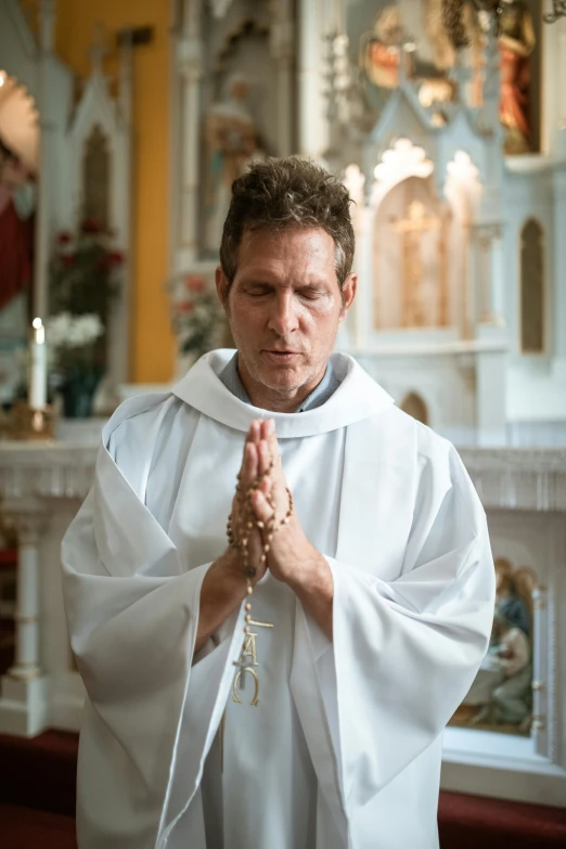 a catholic priest kneeling down and looking at the ground