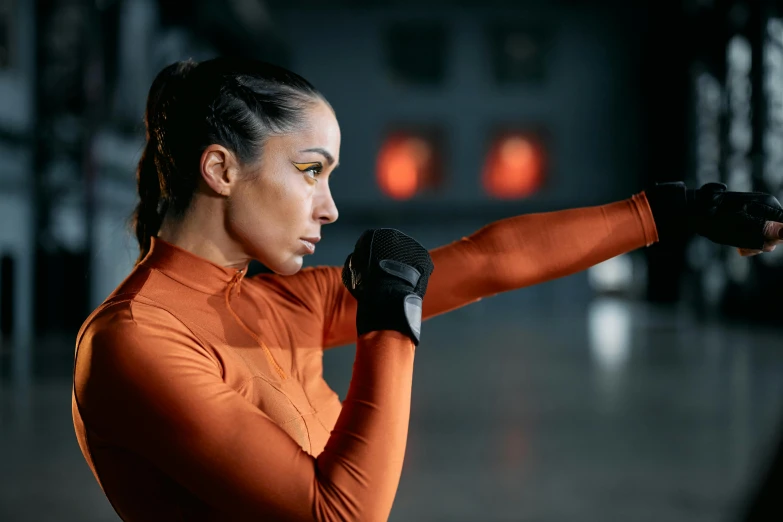 the woman wearing an orange outfit with black gloves is doing exercises