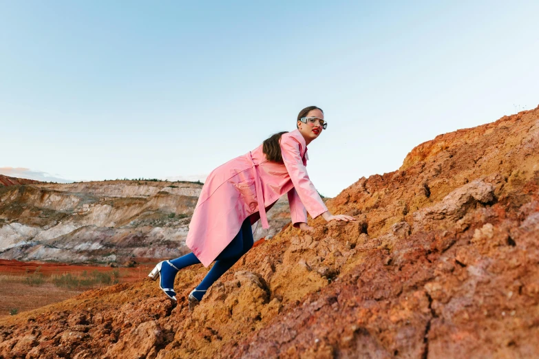 a woman in a pink coat and sunglasses is on some rocks