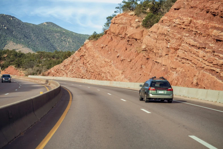 a green car driving down a road near large red mountains