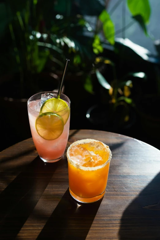 two glasses of various drinks, one containing a margarita and one with a lime