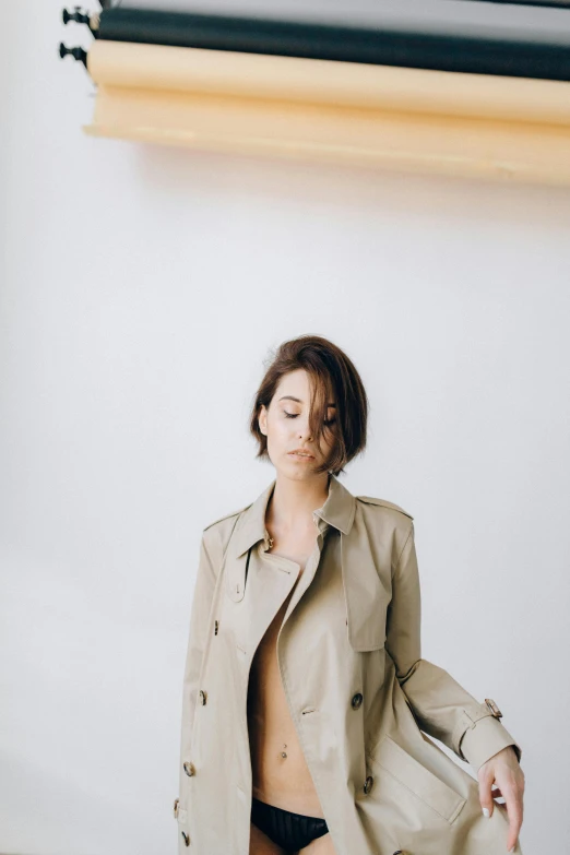 a woman wearing a tan coat and panties poses by a light fixture