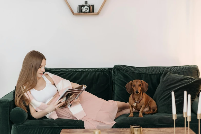 a woman sitting on a green couch next to her dog and holding a book