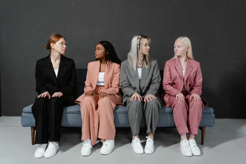 three women sitting on a couch one is wearing white shoes and the other wearing pink