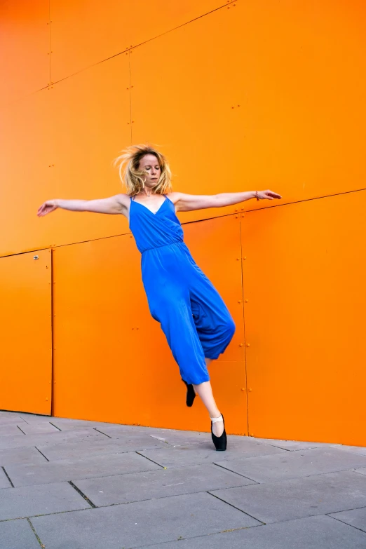 a young woman in blue jumps up against an orange wall