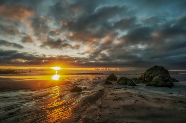 the sun rises above the ocean as the beach is sand covered with sand and rocks