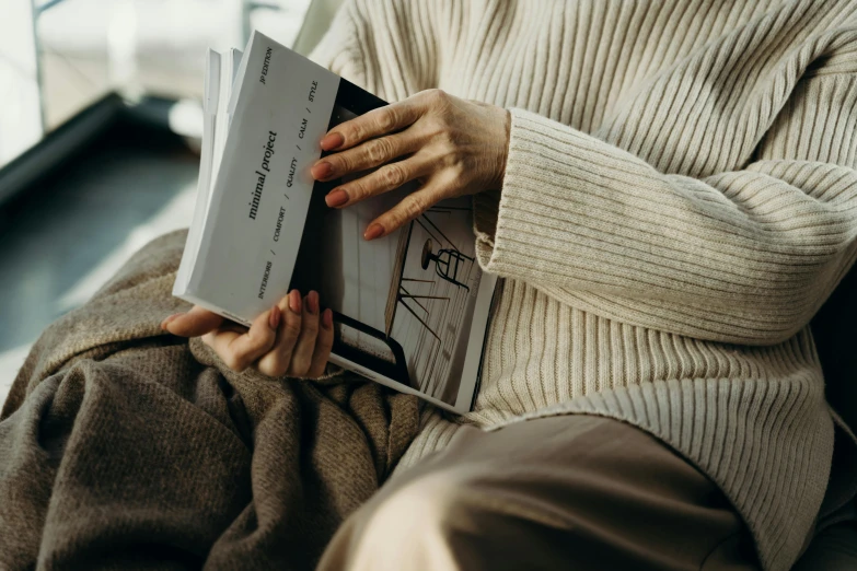 a woman sitting down reading a book on top of her knees