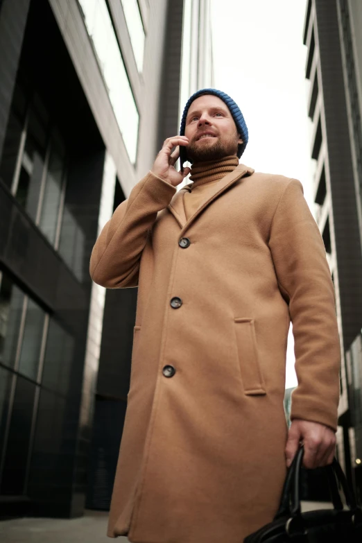 a man in a camel coat is talking on a cellphone