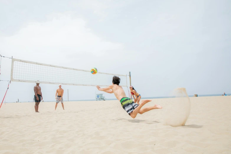 a boy in green shorts and a white shirt playing volleyball on a sandy beach