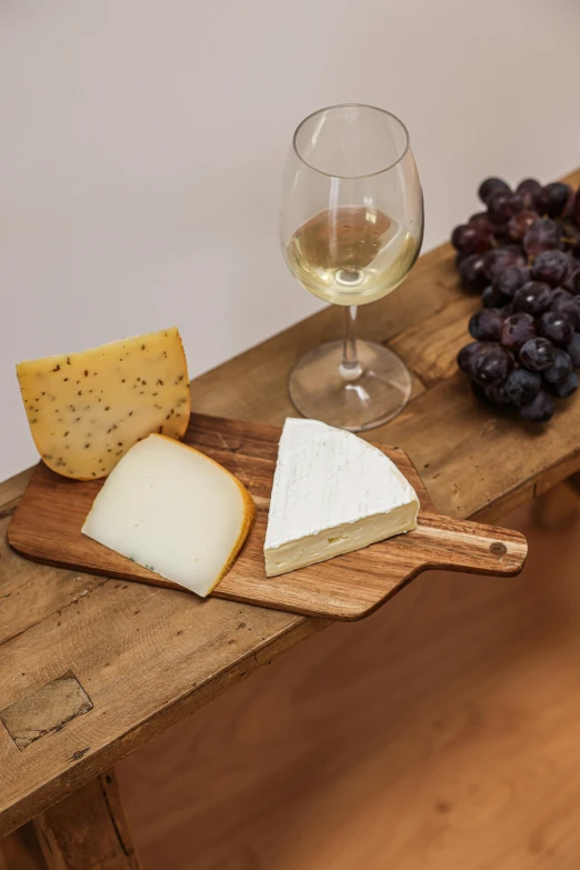 a wine glass sitting next to a  board with a cheese board