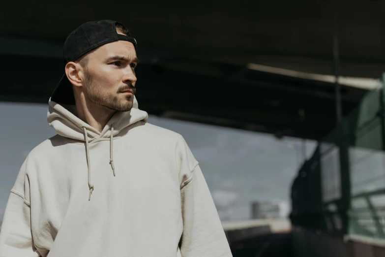 a man with a hat and white shirt and a hoodie standing in front of a train