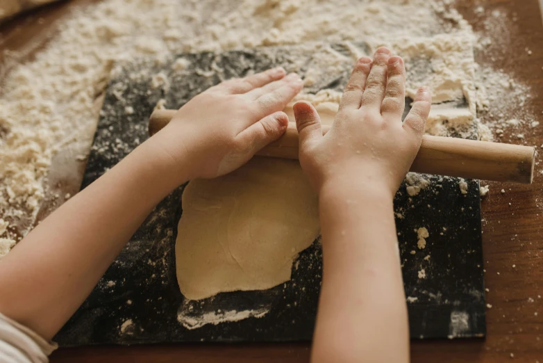 the child is rolling out dough on the counter